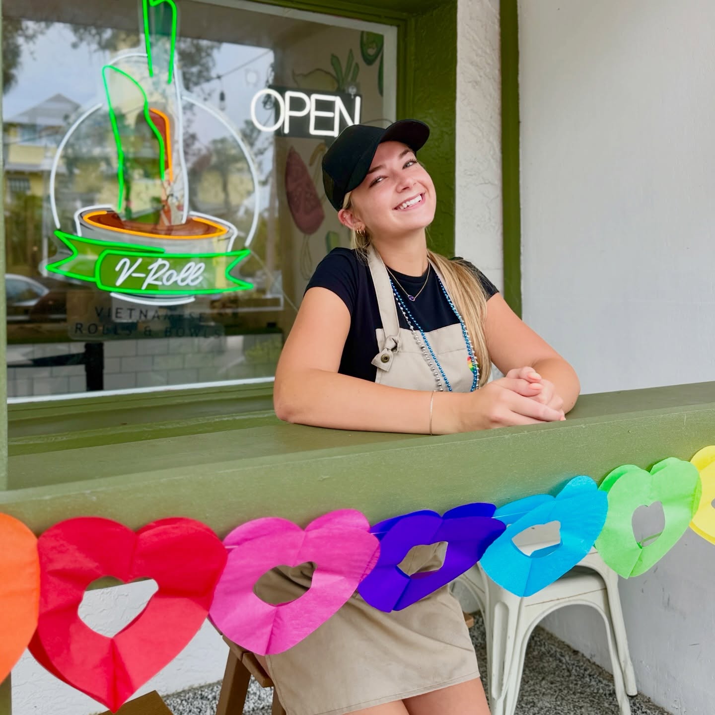 A V-Roll team member smiling at the front window counter beside the OPEN sign