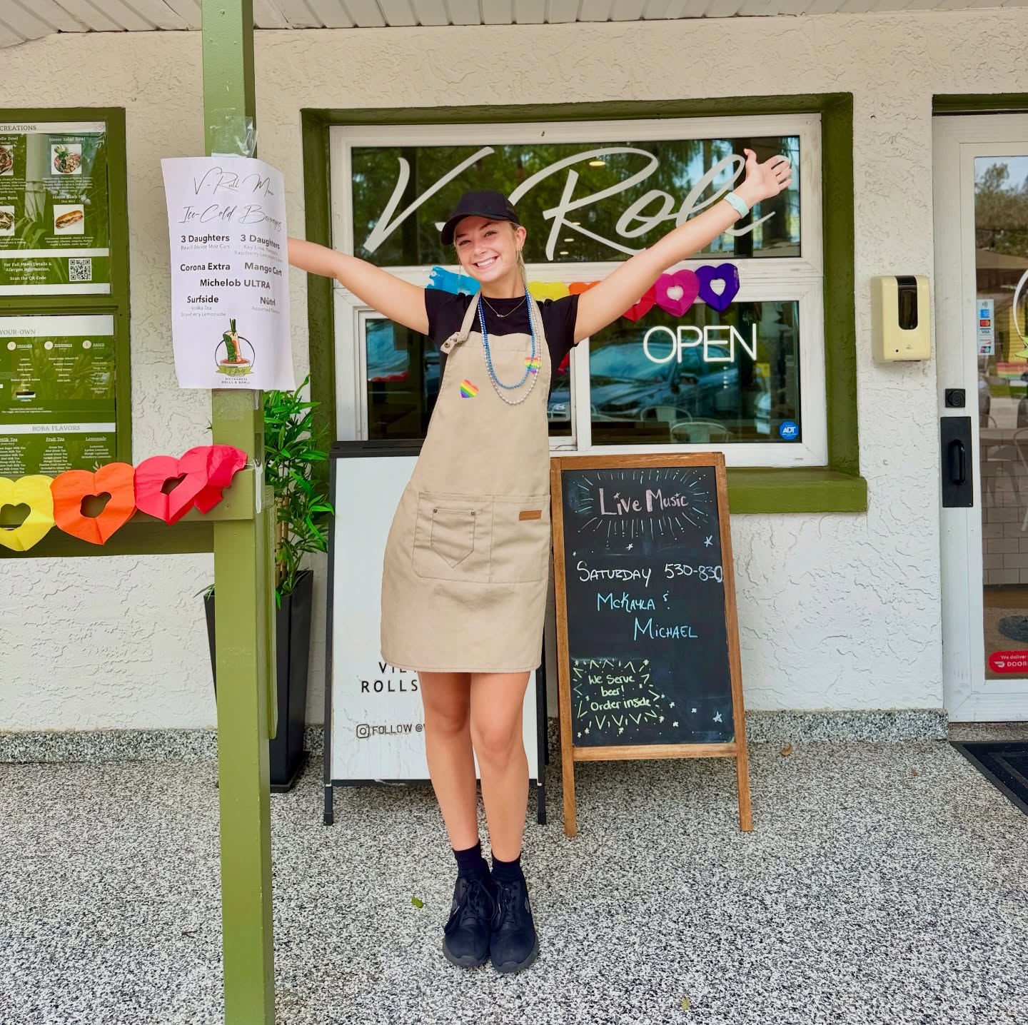 A V-Roll team member with arms wide outside the shop's front door