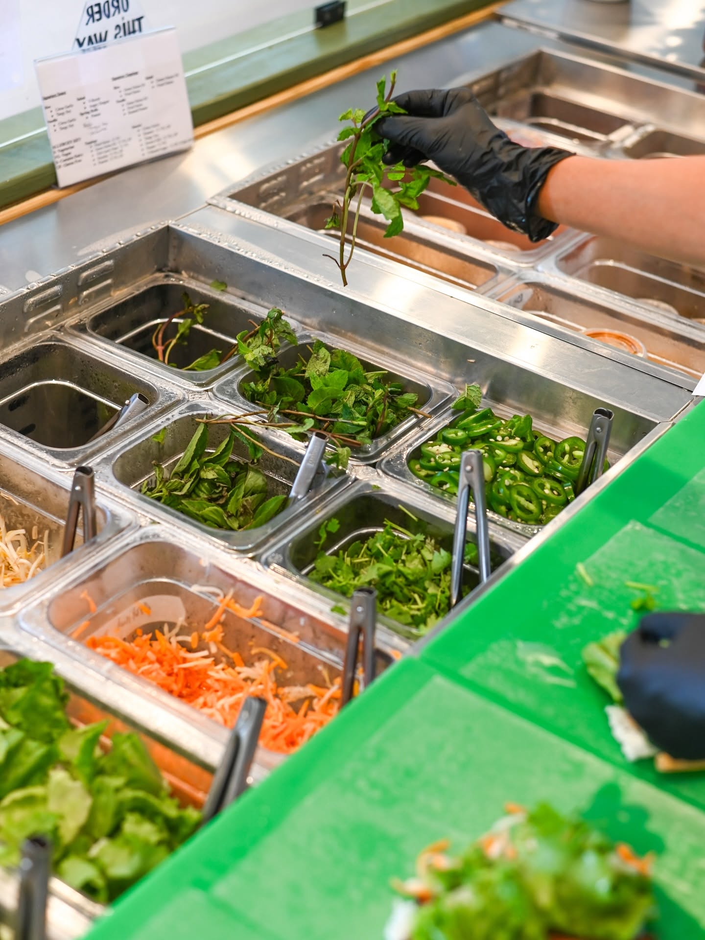 The V-Roll prep line: steel inserts of herbs, lettuce, pickled carrot and noodles behind the green counter