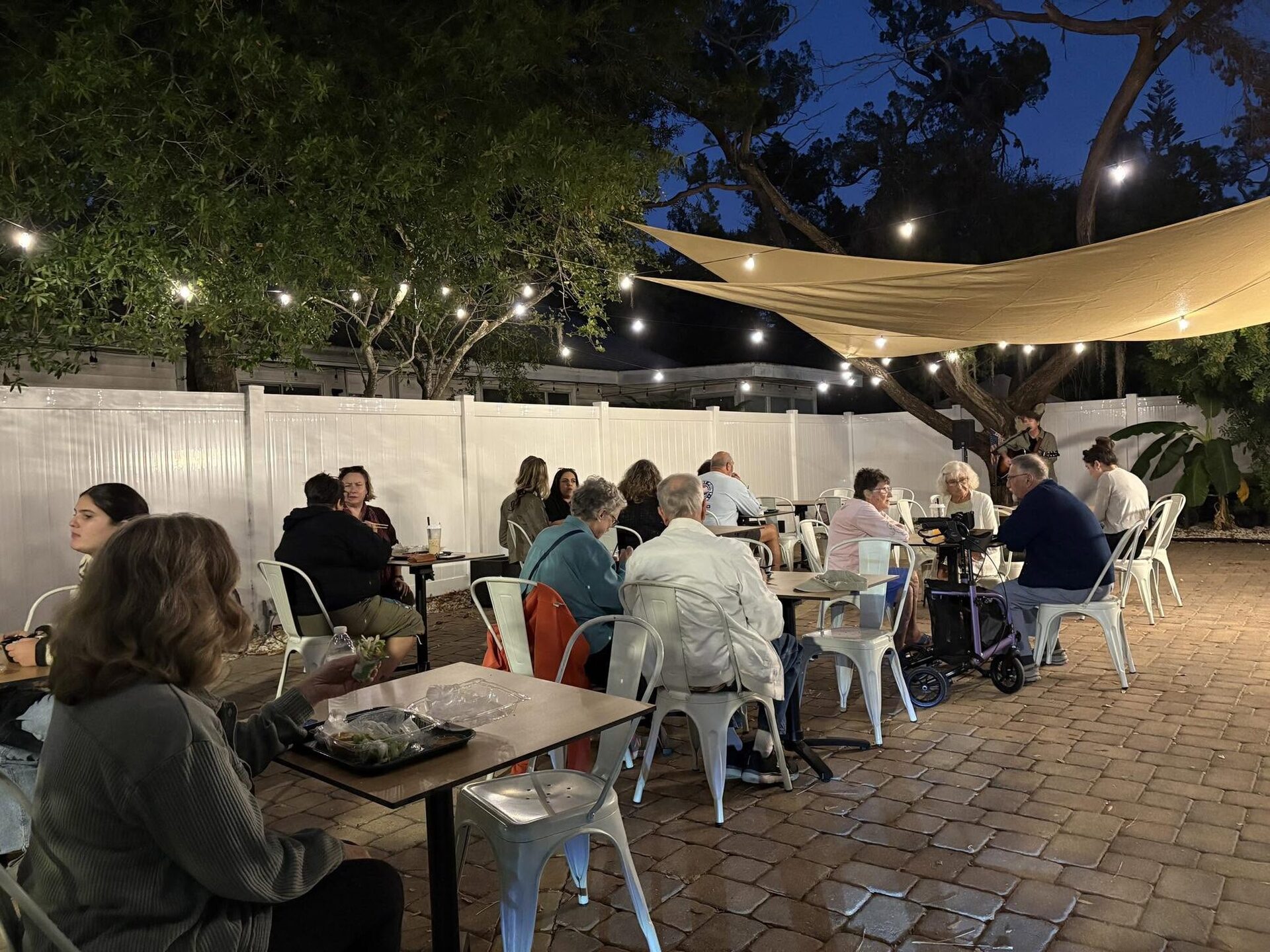 The V-Roll patio at dusk under string lights and shade sails, with diners at every table