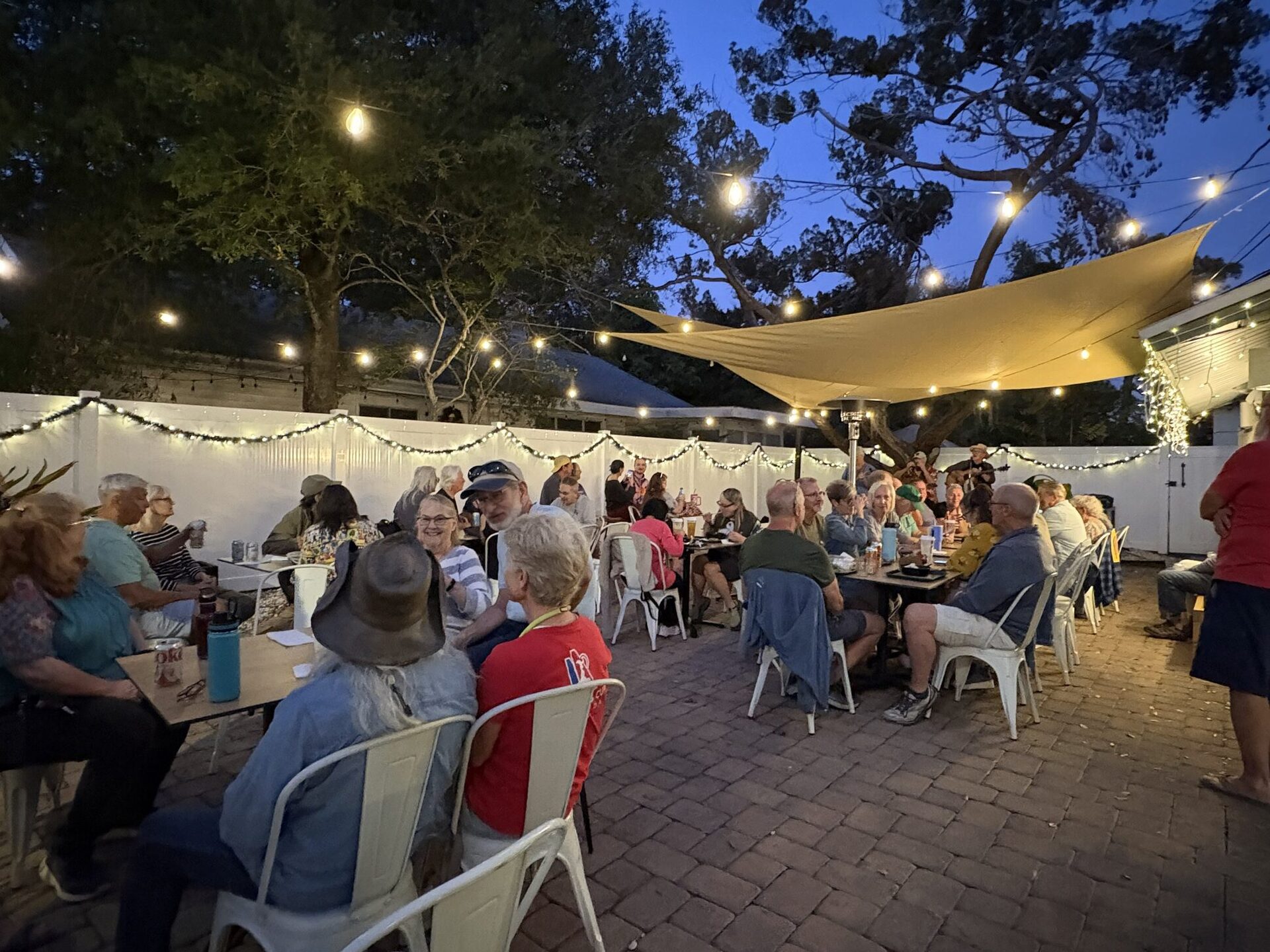 The V-Roll patio at blue hour, string lights overhead and diners at every table