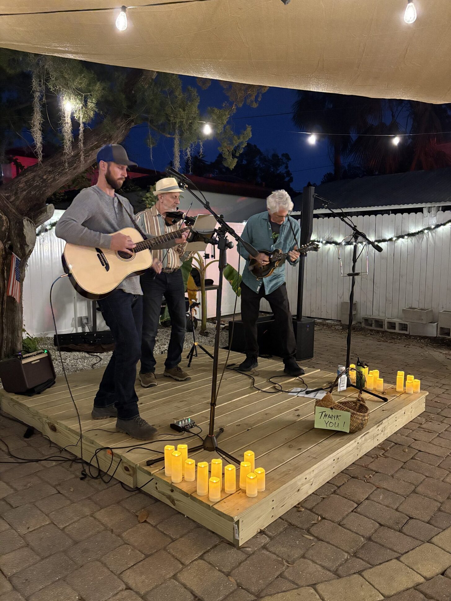 A trio of musicians playing on the patio stage with candles at their feet